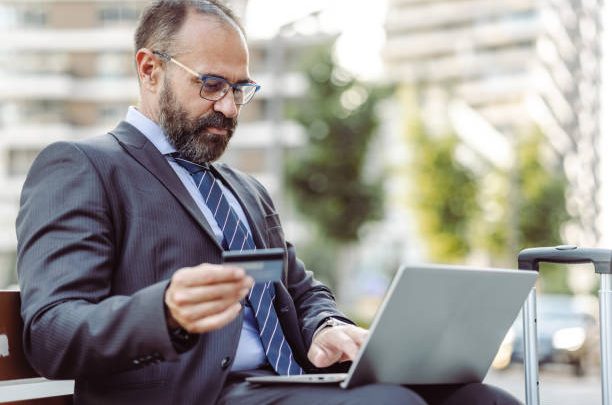 Happy man using laptop and credit card to make flight reservation.